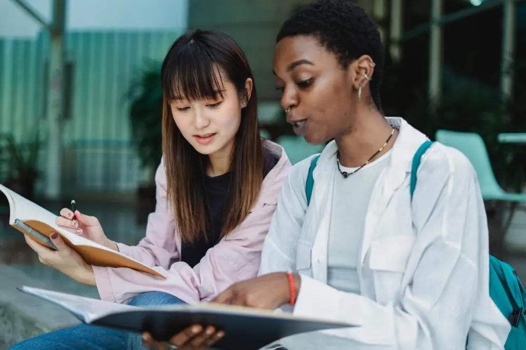 Crop black woman showing book to Asian friend on street